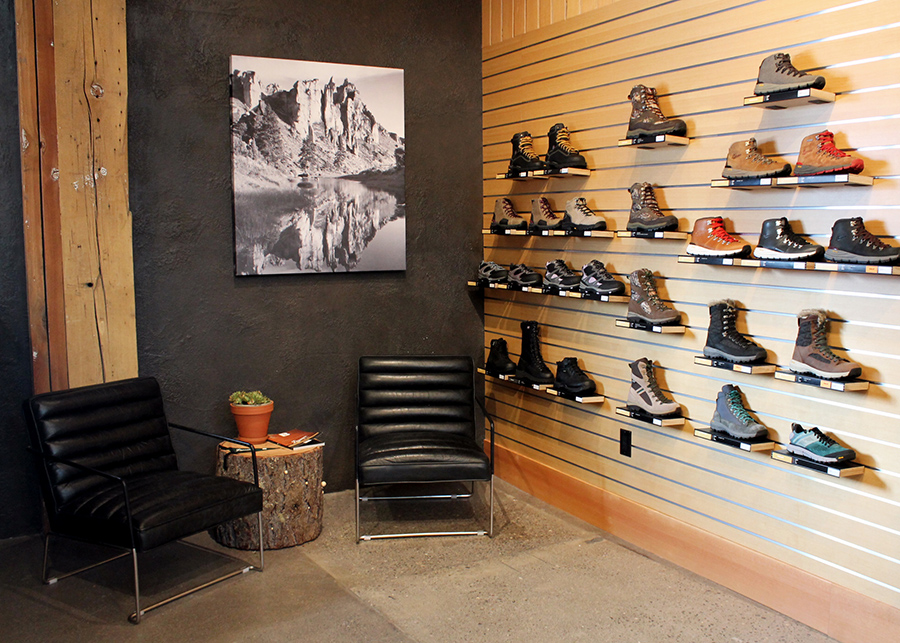 A wood-planked shoe display with metallic inlays,  the try-on area with black leather armchairs, and a tree stump side table